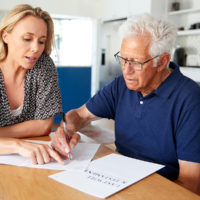 Woman Helping Senior Man To Complete Last Will And Testament At